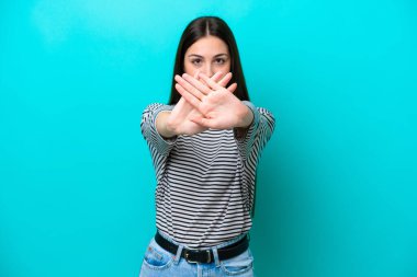 Kafkasyalı genç bir kadın, mavi arka planda izole edilmiş bir şekilde bir eylemi durdurmak için el hareketi yapıyor.