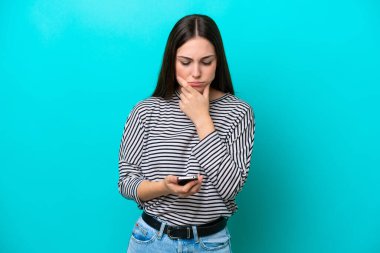 Genç beyaz kadın mavi arka planda izole edilmiş düşünüyor ve bir mesaj gönderiyor.