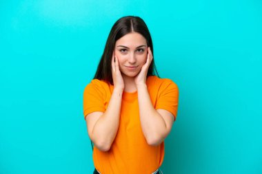 Mavi arka planda izole edilmiş genç beyaz kadın hayal kırıklığına uğramış ve kulaklarını kapatmış.