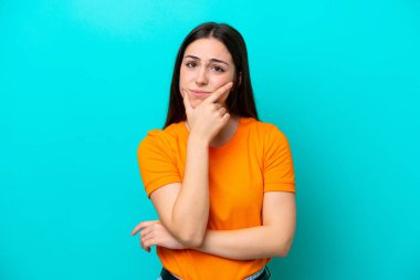 Kafkasyalı genç bir kadın mavi arka planda izole edilmiş. Şüpheleri var.