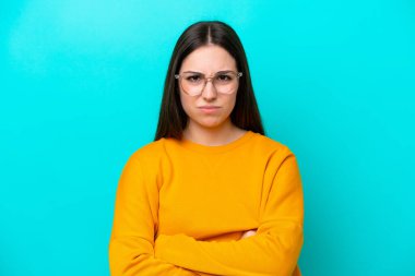 Young girl isolated on blue background With glasses and arms crossed