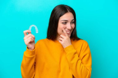 Young caucasian woman holding invisible braces isolated on blue background thinking an idea and looking side