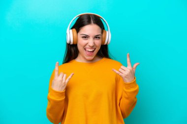 Young girl isolated on blue background listening music making rock gesture