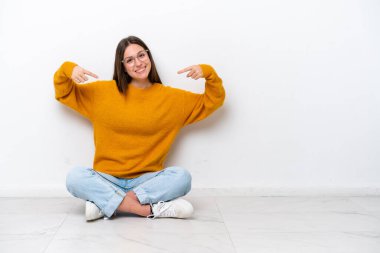 Young girl sitting on the floor isolated on white background proud and self-satisfied