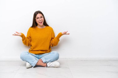 Young girl sitting on the floor isolated on white background with shocked facial expression
