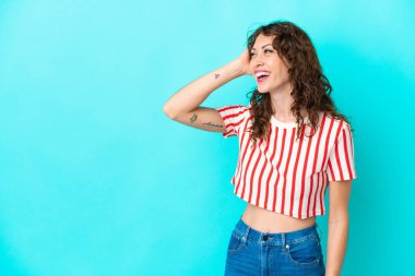 Mavi arka planda izole edilmiş kıvırcık saçlı genç bir kadın çok gülümsüyor.