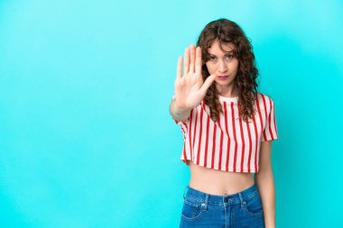 Mavi arka planda, kıvırcık saçlı genç bir kadın dur hareketi yapıyor.