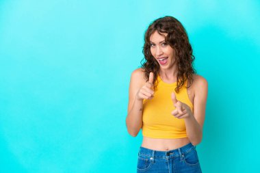 Mavi arka planda izole edilmiş kıvırcık saçlı ve gülümseyen genç bir kadın.