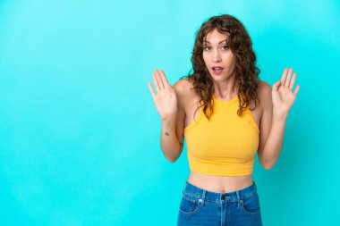Mavi arka planda, kıvırcık saçlı, kuşkulu hareketler yapan genç bir kadın.