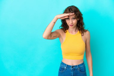 Mavi arka planda yalıtılmış kıvırcık saçlı genç bir kadın bir şeye bakmak için uzaklara bakıyor.