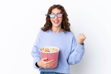 Beyaz arka planda üç boyutlu gözlüklü ve elinde koca bir kova patlamış mısır tutan kıvırcık saçlı genç bir kadın.