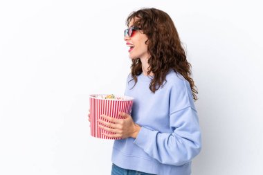 Beyaz arka planda üç boyutlu gözlüklü ve elinde koca bir kova patlamış mısır tutan kıvırcık saçlı genç bir kadın.