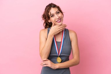 Pembe arka planda madalyalı genç beyaz kadın gülümsüyor.
