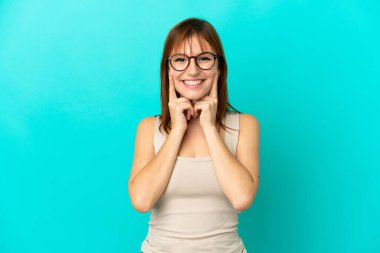 Kızıl saçlı kız mavi arka planda yalnız mutlu ve hoş bir ifadeyle gülümsüyor.