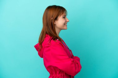 Madalyaları olan kızıl saçlı kız mavi arka planda yan pozisyonda.