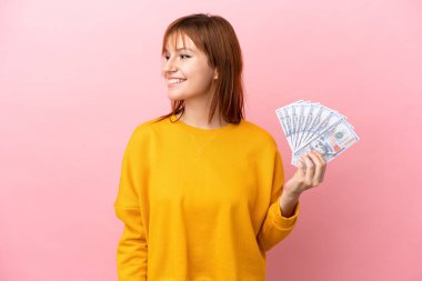 Kızıl saçlı kız çok para alıyor. Pembe arka planda izole edilmiş.
