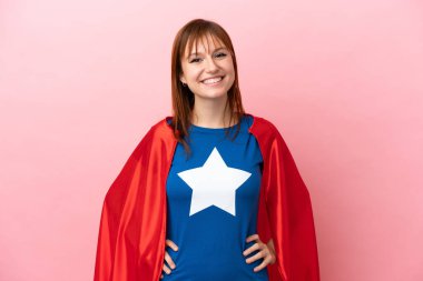 Süper kahraman kızıl saçlı kız pembe arka planda yalnız gülüyor.