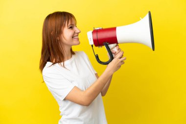 Sarı arka planda izole edilmiş kızıl saçlı bir kız megafondan bir şey duyurmak için bağırıyor.