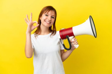 Sarı arka planda izole edilmiş kızıl saçlı bir kız elinde bir megafonla tamam işaretini parmaklarıyla gösteriyor.