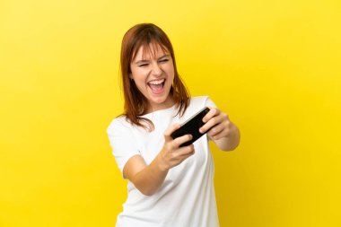 Sarı arka planda izole edilmiş kızıl saçlı kız cep telefonuyla oynuyor.