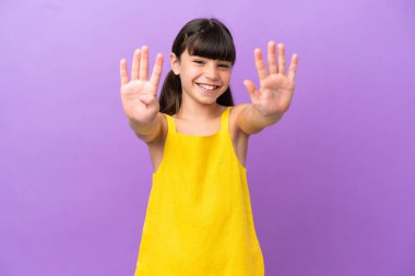Mor arka planda izole edilmiş küçük beyaz çocuk parmaklarıyla dokuz tane sayıyor.