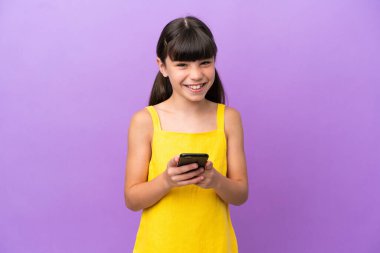 Mor arka planda izole edilmiş küçük beyaz çocuk cep telefonuyla bir mesaj gönderiyor.