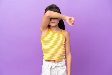 Mor arka planda izole edilmiş küçük beyaz çocuk gözleri elleriyle kapatıyor.