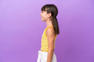 Küçük beyaz çocuk, mor arka planda izole edilmiş. Yan pozisyonda gülüyor.