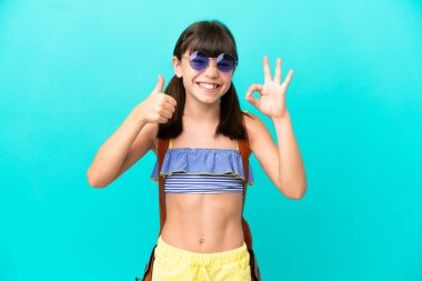 Küçük beyaz bir çocuk kumsala gidiyor. Mavi arka planda izole edilmiş. Tamam işareti gösteriyor.