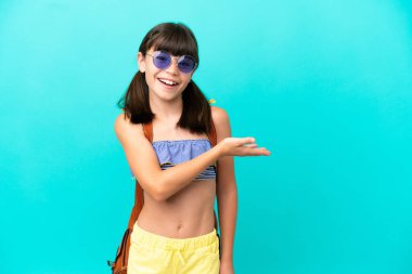 Küçük beyaz bir çocuk kumsala gidiyor. Mavi arka planda tek başına. Bir fikir sunuyor ve gülümsüyor.