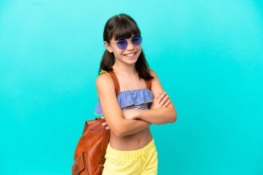 Küçük beyaz bir çocuk kumsala gidiyor. Mavi arka planda izole edilmiş, kolları bağlı ve ileriye bakıyor.