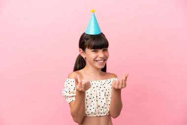 Doğum günü şapkalı küçük beyaz çocuk pembe arka planda izole edilmiş para hareketi yapıyor.