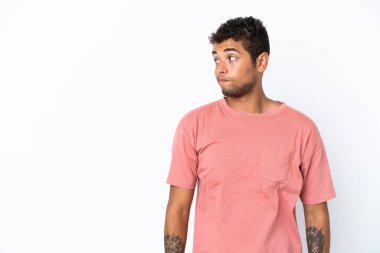 Beyaz arka planda izole edilmiş yakışıklı Brezilyalı adam şüpheli hareketler yapıyor.