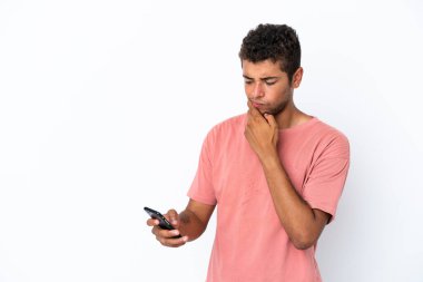 Genç ve yakışıklı Brezilyalı bir adam beyaz arka planda izole edilmiş düşünüyor ve bir mesaj gönderiyor.
