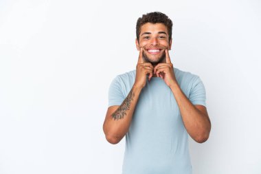 Genç, yakışıklı Brezilyalı bir adam beyaz arka planda izole edilmiş mutlu ve hoş bir ifadeyle gülümsüyor.