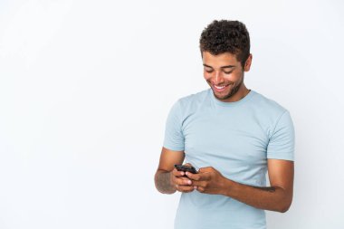 Beyaz arka planda izole edilmiş yakışıklı Brezilyalı genç cep telefonuyla bir mesaj gönderiyor.