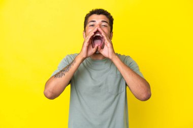 Genç, yakışıklı Brezilyalı bir adam sarı arka planda izole edilmiş bağırıyor ve bir şeyler söylüyor.