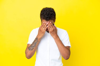 Genç yakışıklı Brezilyalı adam, sarı arka planda izole edilmiş, yorgun ve hasta bir ifadeyle.