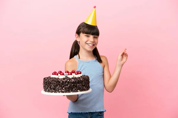 Little caucasian kid holding birthday cake isolated in pink background pointing back