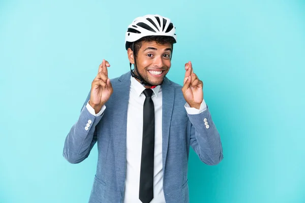 Young business Brazilian man with bike helmet isolated on blue background with fingers crossing