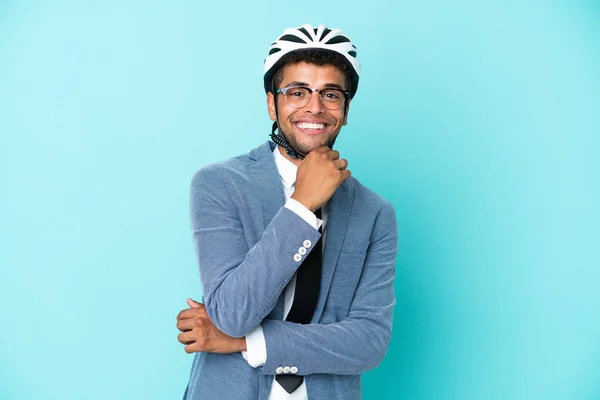 Young business Brazilian man with bike helmet isolated on blue background with glasses and smiling
