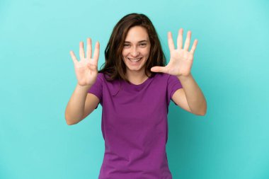 Mavi arka planda izole edilmiş genç beyaz kadın parmaklarıyla dokuzu sayıyor.