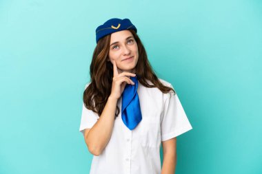 Uçak hostesi kadın mavi arka planda izole edilmiş, yukarı bakarken bir fikir düşünüyor.