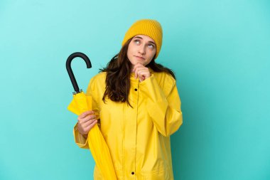 Mavi arka planda şemsiye tutan genç beyaz bir adam var.