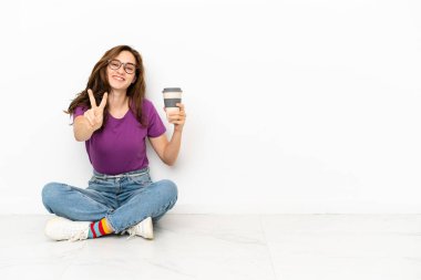 Beyaz arka planda izole edilmiş genç beyaz kadın gülümsüyor ve zafer işareti gösteriyor.