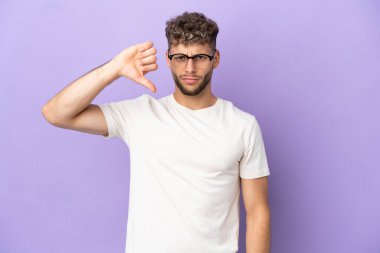 Mor arka planda izole edilmiş beyaz bir adam negatif ifadeyle baş parmağını aşağı gösteriyor.