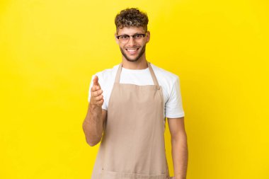 Restoran garsonu. Sarışın adam sarı arka planda izole edilmiş. İyi bir anlaşma için el sıkışıyor.