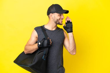 Sarı arka planda izole edilmiş spor çantalı genç sarışın adam ağzı sonuna kadar açık bağırıyor.