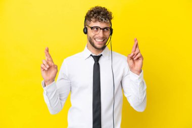 Tele pazarlamacı sarışın adam sarı arka planda izole edilmiş kulaklıkla çalışıyor.