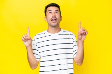 Genç yakışıklı, izole edilmiş sarı arka plan şaşırmış ve yukarı bakıyor.